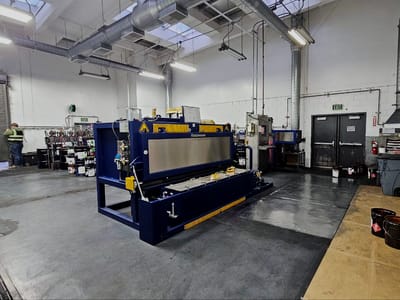 Press brake standing in the middle of the shop bay with its back gauge set, and welding bays and benches running along the far wall.