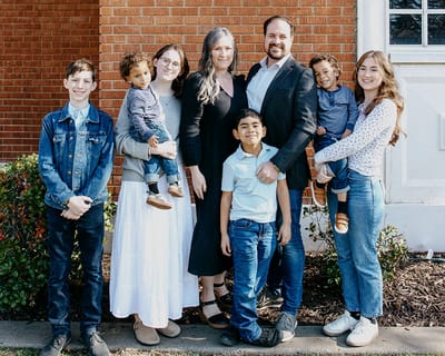 The Miller family standing together outside their church, against a red brick wall with tall white-framed windows — the family behind Miller 3 Engineering.