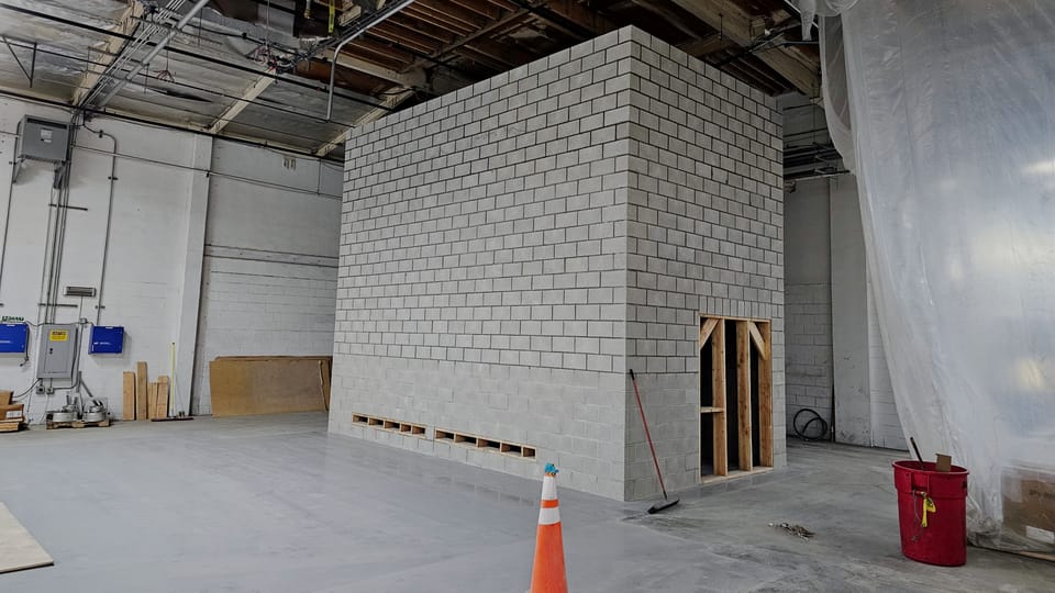 Hazardous-area enclosure at mid-build, concrete block walls laid to about two-thirds height with a timber-framed opening and pallets of block inside.