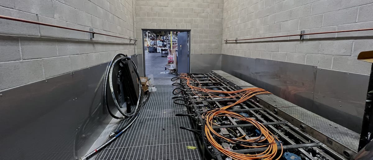 Interior of a hazardous-area enclosure, block walls to both sides and a bar-grating deck carrying conduit runs and coiled orange service leads.