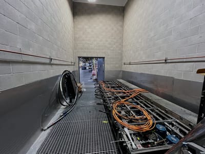 Interior of a hazardous-area enclosure, block walls to both sides and a bar-grating deck carrying conduit runs and coiled orange service leads.