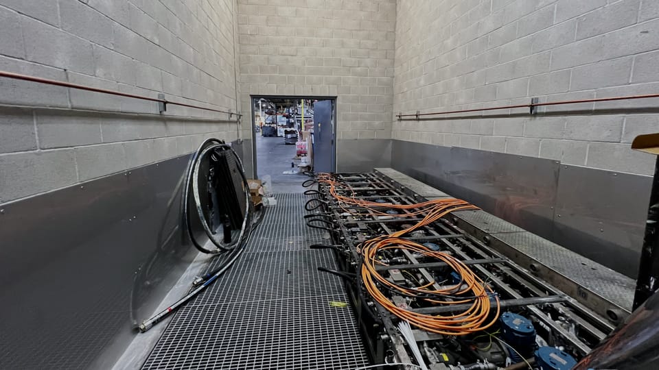Interior of a hazardous-area enclosure, block walls to both sides and a bar-grating deck carrying conduit runs and coiled orange service leads.
