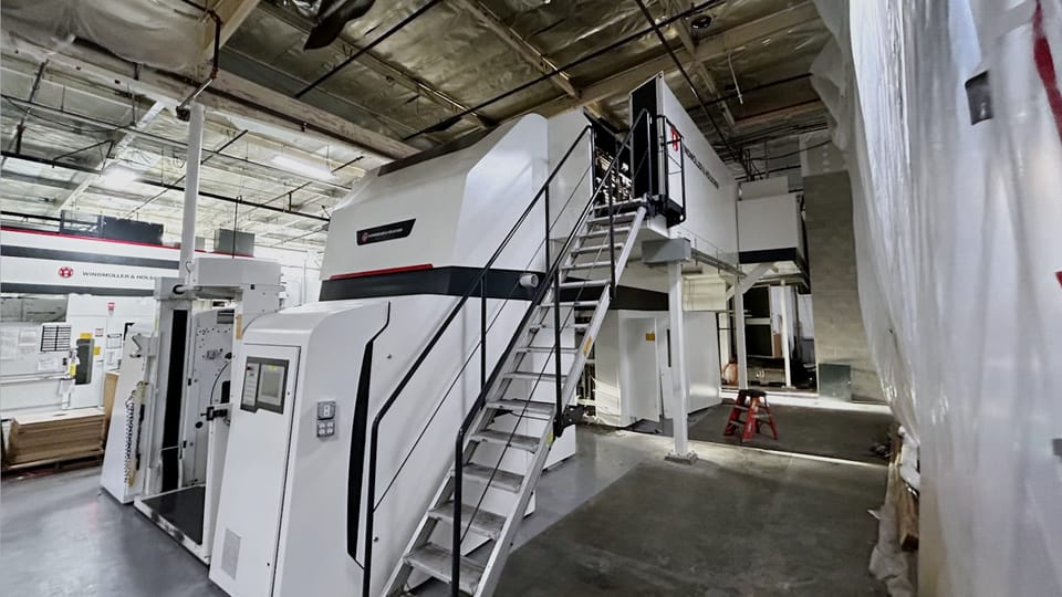 OEM press line set on a plant floor behind temporary containment sheeting, with a fabricated steel access stair and platform on its left flank.