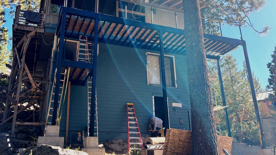 Side elevation of the finished deck structure, steel columns landing on new concrete piers with the balcony framing cantilevered past the wall.