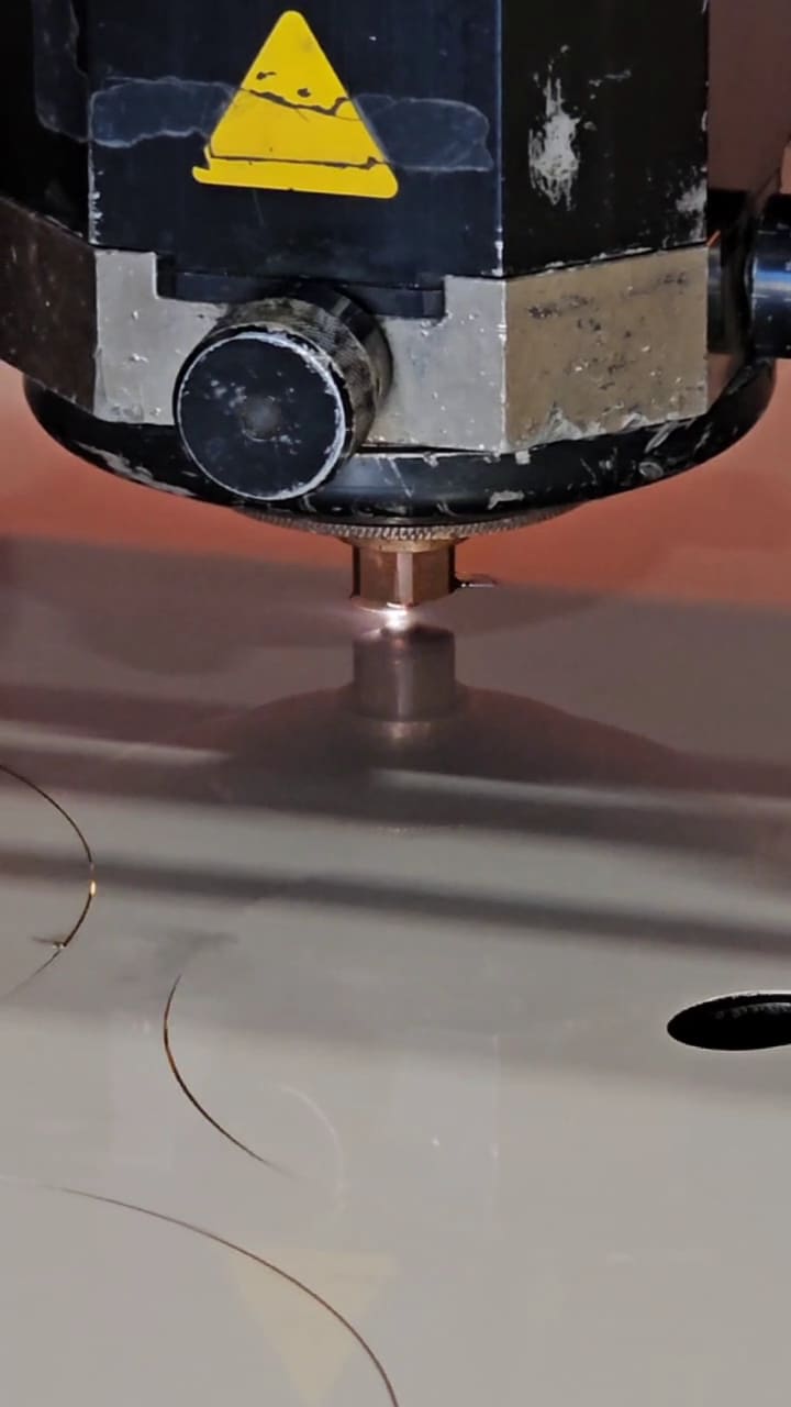 Fiber laser head tracking across steel plate, cutting a circular blank with the kerf glowing behind the nozzle.